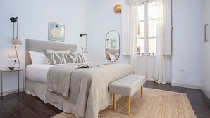 A bedroom with a bed, bedside tables, a bench, a mirror, and a window with curtains. - Luxury Apartment in Malaga Larios VI (Málaga)
