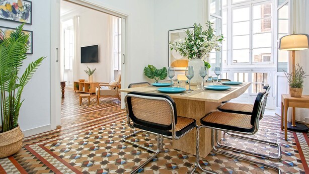 A dining area with a geometric patterned floor, a wooden table, and modern chairs. - Luxury Apartment in Malaga Larios VI (Málaga)