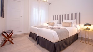 Ein Doppelbett mit gestreifter Kopfteil, ein Nachttisch mit Lampe und ein Fenster mit transparenten Vorhängen.