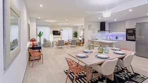 Eine moderne Küche mit Einbauofen und Kühlschrank, ein Essbereich mit Holztisch und Stühlen sowie ein Wohnzimmer mit Sofa und Fernseher.