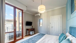 Quarto com cama, escrivaninha, televisão e porta de vidro deslizante para uma varanda.