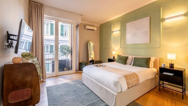 Quarto de hotel com uma cama grande, uma mesa com cadeira, varanda com vista e uma obra de arte pendurada na parede.