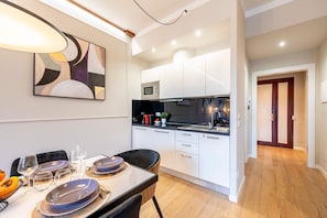 A modern kitchen with white cabinets, a microwave, and a sink. There is a dining table with plates and glasses. - Central 3BD Apartment Near Teatro Verdi (Florence)