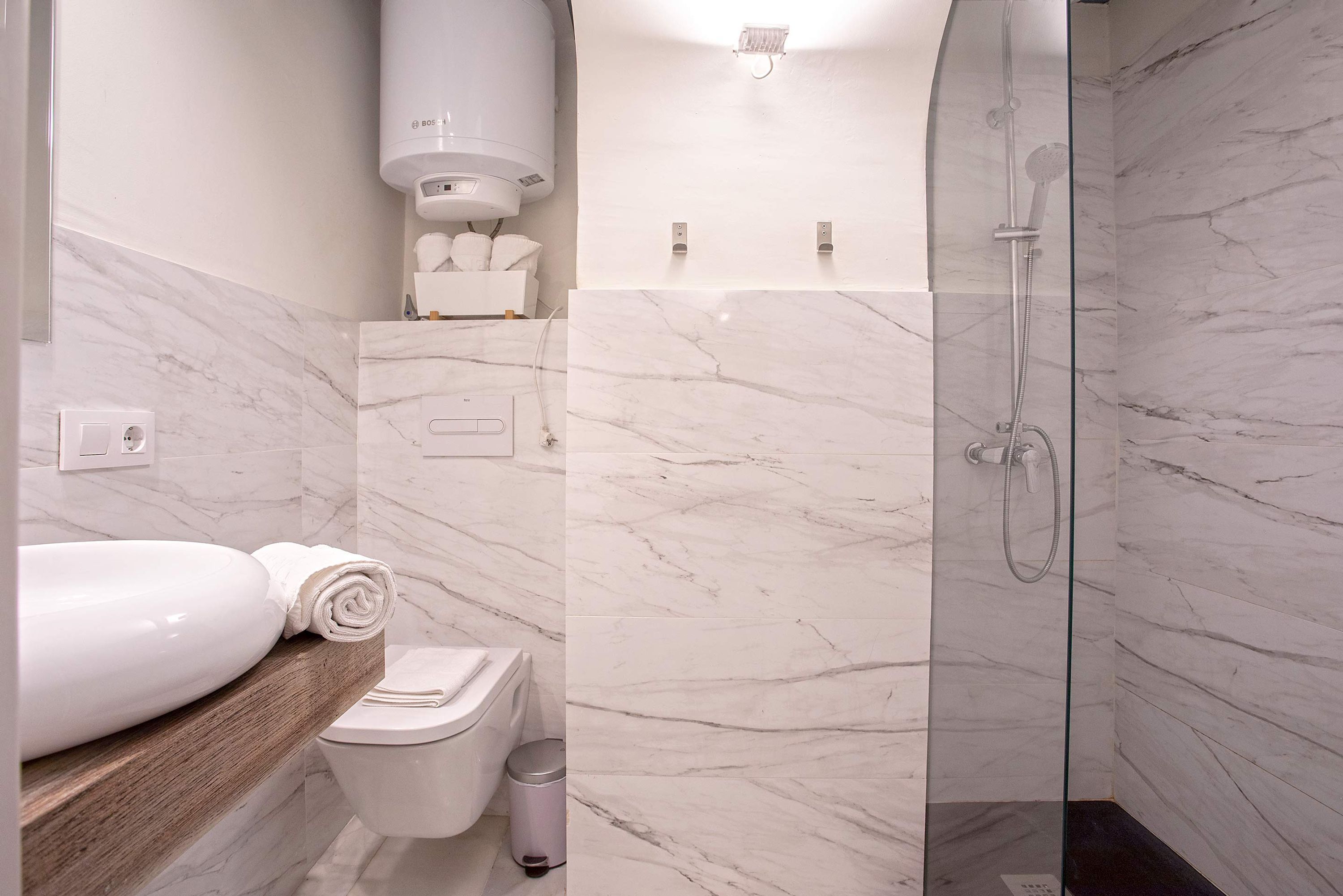 A modern bathroom with a marble floor, a glass-enclosed shower, a toilet, and a sink with a wooden countertop.