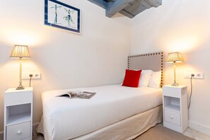 A neatly made bed with a red pillow, two bedside tables with lamps, and a framed artwork above the bed. - Luxury Apartament in Seville San Isidoro II (Seville)