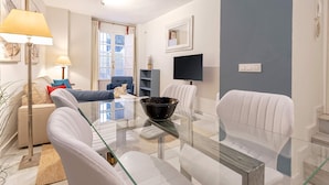 Un salon moderne avec une table basse en verre, des canapés en cuir blanc, un fauteuil bleu et un téléviseur fixé au mur.
