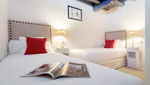 Une chambre d’hôtel avec deux lits, chacun agrémenté d’un oreiller rouge, de draps blancs et de lampes de chevet. Un magazine est ouvert sur l’un des lits.