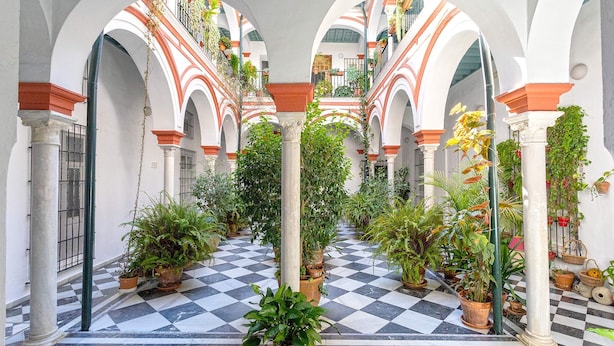 Une cour avec un sol à carreaux, des arches, des colonnes et des plantes en pot.