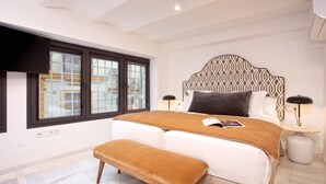 A modern bedroom with a large bed, a bench, a patterned headboard, and a window with blinds. - Cozy 2BD Duplex in Seville Center Gran Poder (Seville)