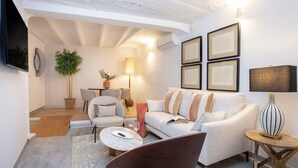 A modern living room with a white sofa, a brown armchair, a coffee table, and a lamp. There is a staircase leading to an upper level, and a potted plant is visible. - Cozy 2BD Duplex in Seville Center Gran Poder (Seville)