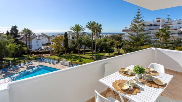 Un balcon avec une piscine, des meubles blancs et une table dressée pour le repas.