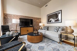 Una sala de estar moderna con pared de ladrillo, televisor de pantalla plana, sofá gris, mesa de centro redonda y alfombra estampada.