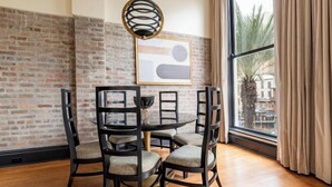 A dining area with a brick wall, a round table, and four chairs. - 2BR Luxury Stay & Stunning City Views The Mayfair (New Orleans)