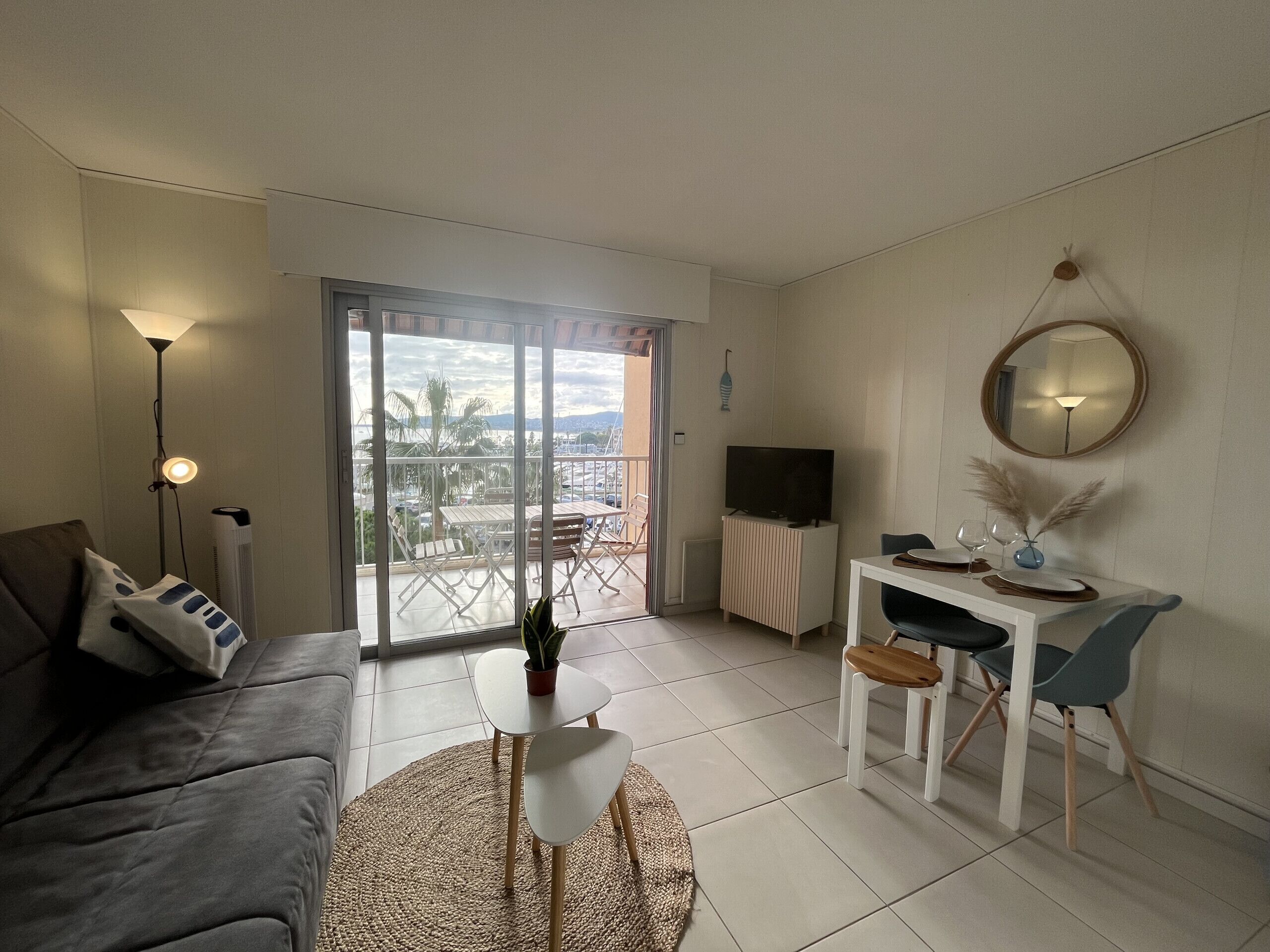 A living room with a sofa, a coffee table, a TV on a stand, a dining table with chairs, and a balcony with a view.