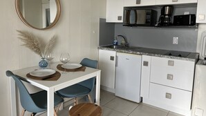 A compact kitchen with white cabinets, a microwave, and a coffee maker. There is a dining table with two chairs and a small round table with a plate and a glass. - The Capitole, Studio 26m2, air-conditioned, sea view, balcony, WIFI, parking for 2 adults and 2 children (Fréjus)