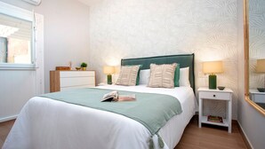 Un dormitorio ordenado con una cama grande, dos mesitas de noche, una mesita auxiliar, un ventanal y un espejo.