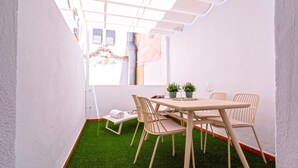 Un pequeño espacio al aire libre amurallado con mesa y sillas, un banco y una planta en maceta.
