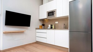 Una cocina moderna con armarios blancos, un refrigerador de acero inoxidable, un microondas y un televisor de pantalla plana montado en la pared.