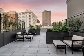 Une terrasse sur le toit avec des sièges en plein air, une vue sur les toits de la ville et un bâtiment moderne en arrière-plan.