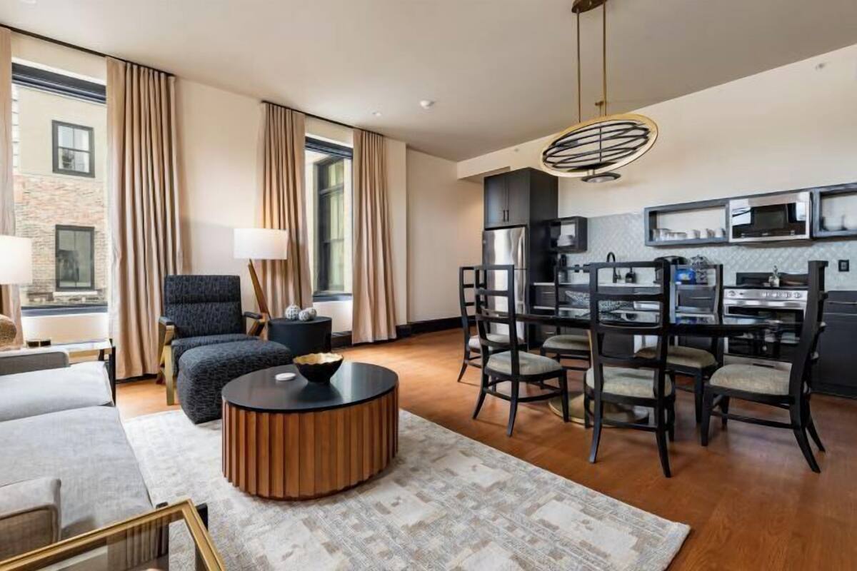 A modern hotel room with a living area, dining space, and kitchen.
