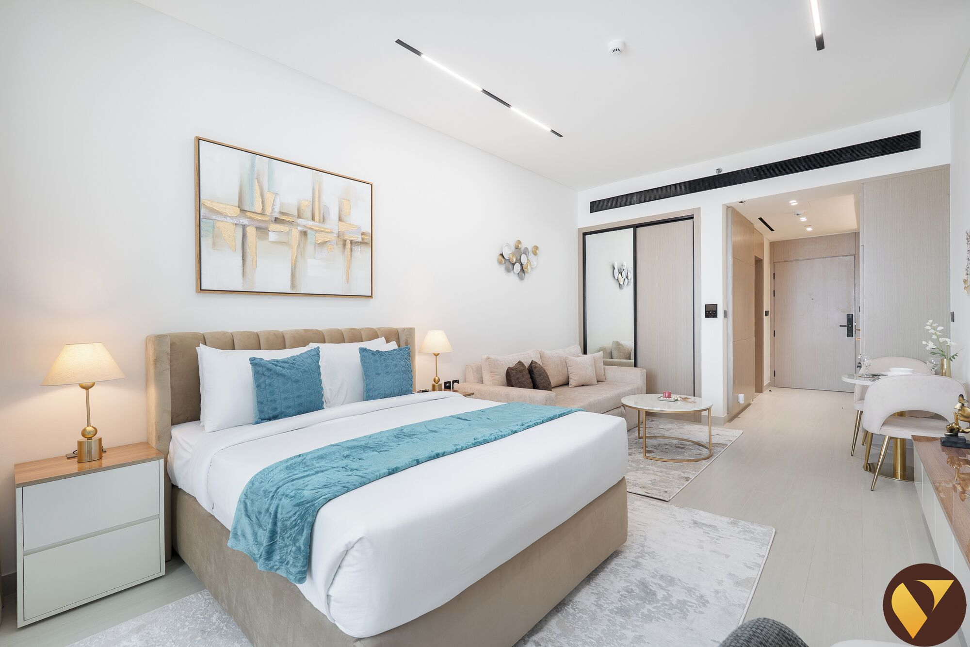 A modern hotel room with a large bed, bedside tables, a sofa, a small table, and a mirror.