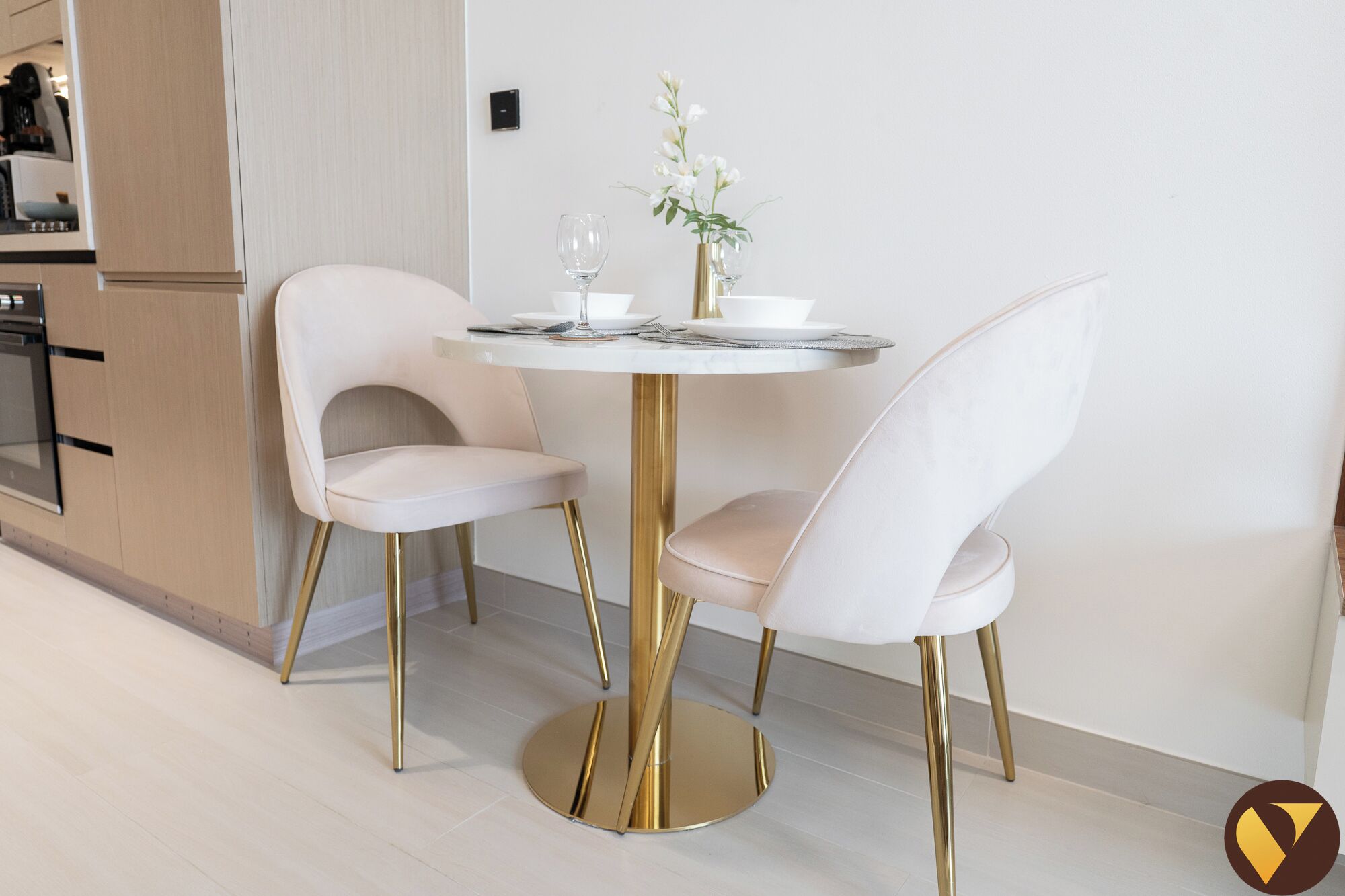Un'area pranzo moderna con un tavolo rotondo e due sedie bianche dalle gambe dorate.