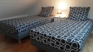 Two single beds with patterned bedding, a nightstand with a lamp, and a wooden floor. - Cottage 'Le Gîte D’Ambre' with Private Garden and Wi-Fi (Poullaouen)