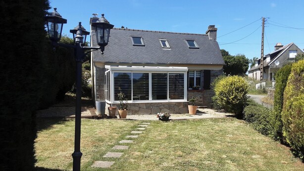 A house with a stone facade, a conservatory with glass doors, and a paved garden area with stepping stones. - Cottage 'Le Gîte D’Ambre' with Private Garden and Wi-Fi (Poullaouen)