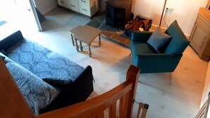A living room with a sofa, a chair, a small table, a fireplace, and a lamp. - Cottage 'Le Gîte D’Ambre' with Private Garden and Wi-Fi (Poullaouen)