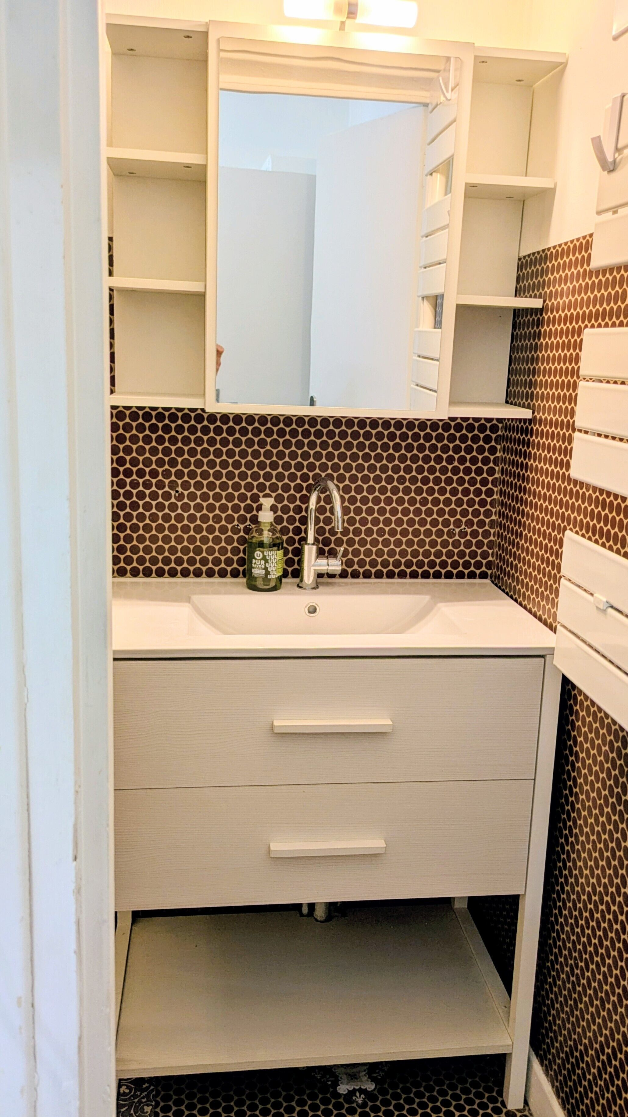 A bathroom with a sink, mirror, and a bottle of hand soap.