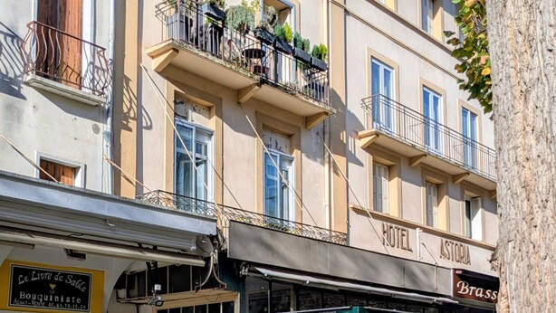 Un edificio de varios pisos con balcones con plantas, un restaurante en la planta baja y una tienda visible con señalización.