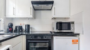 Una cocina con armarios blancos, una estufa negra, un microondas y una cafetera.