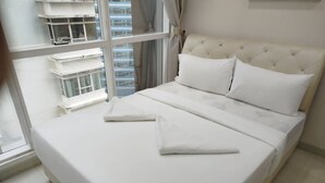 Un lit bien fait, avec du linge de lit blanc et des oreillers, une tête de lit capitonnée et une vue sur le paysage urbain à travers de grandes fenêtres.
