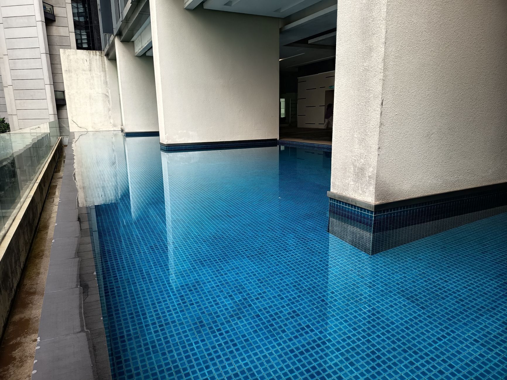 A swimming pool with a tiled floor and a glass barrier on one side.