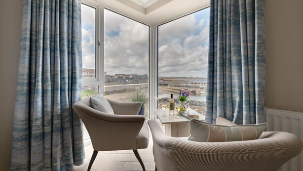 Ein Zimmer mit Blick auf eine Küstenlandschaft, ausgestattet mit zwei Sesseln und einem kleinen Tisch mit Flasche und Gläsern.