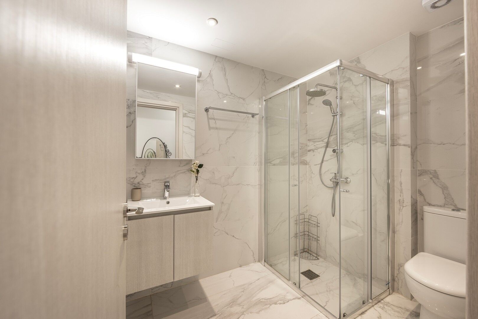 Une salle de bain moderne avec une douche à parois de verre, un sol carrelé en marbre et des toilettes blanches.
