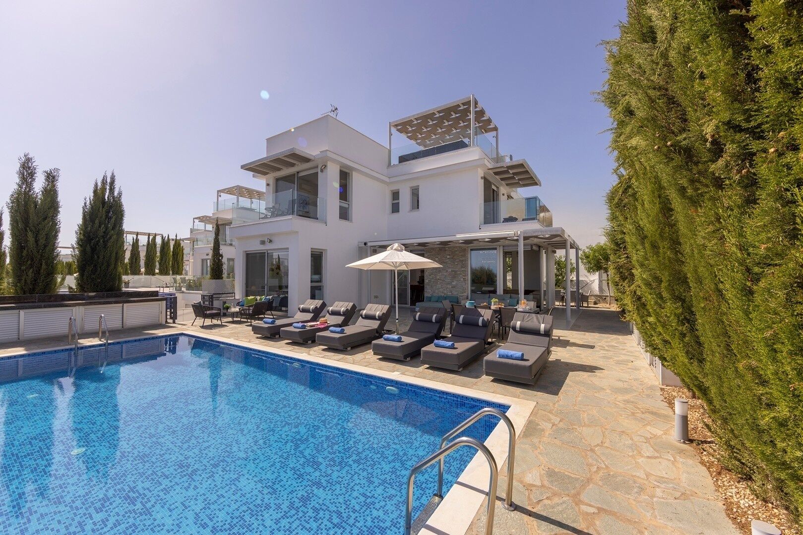 A modern two-story house with a swimming pool, sun loungers, and a covered outdoor seating area.