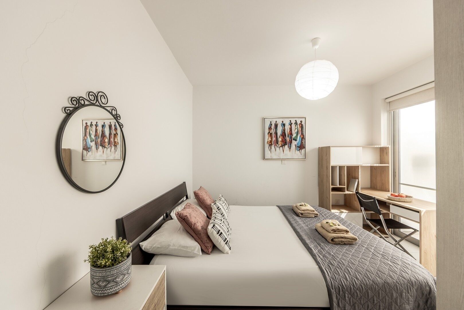 A modern bedroom with a bed, bedside table, potted plant, and artwork on the walls.