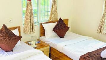 A hotel room with two single beds, a wooden headboard, a window with curtains, and a bedside table with a lamp.