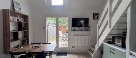 A compact kitchen with a dining area, a TV mounted above the counter, and a staircase leading to an upper level.