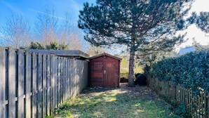 Une clôture en bois, un abri de jardin rouge et un grand arbre dans une cour arrière.