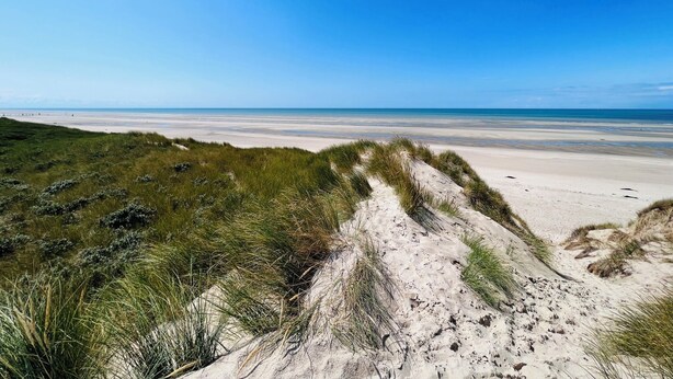 Une plage avec des dunes de sable et un ciel bleu azur.