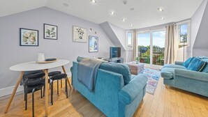 A modern living room with a blue sofa, a white table with chairs, and artwork on the walls. - Charming Village Escape near Loch Lomond (Drymen)