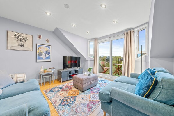 A modern living room with a TV, sofa, and a large window. - Charming Village Escape near Loch Lomond (Drymen)