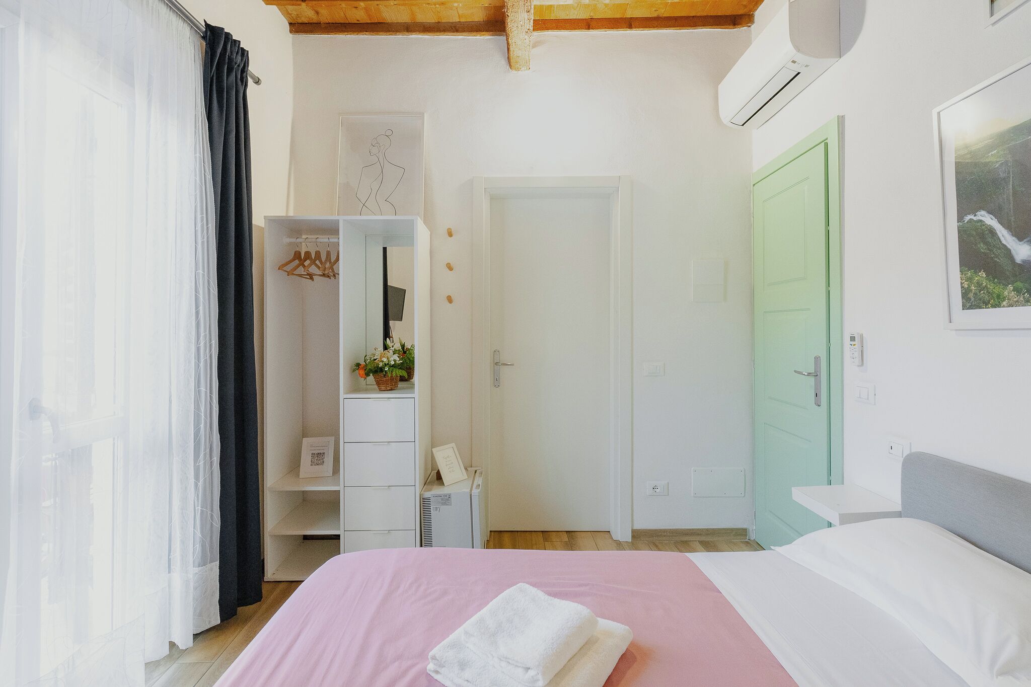 A bedroom with a bed, a wardrobe, a mirror, a green door, and an air conditioning unit.