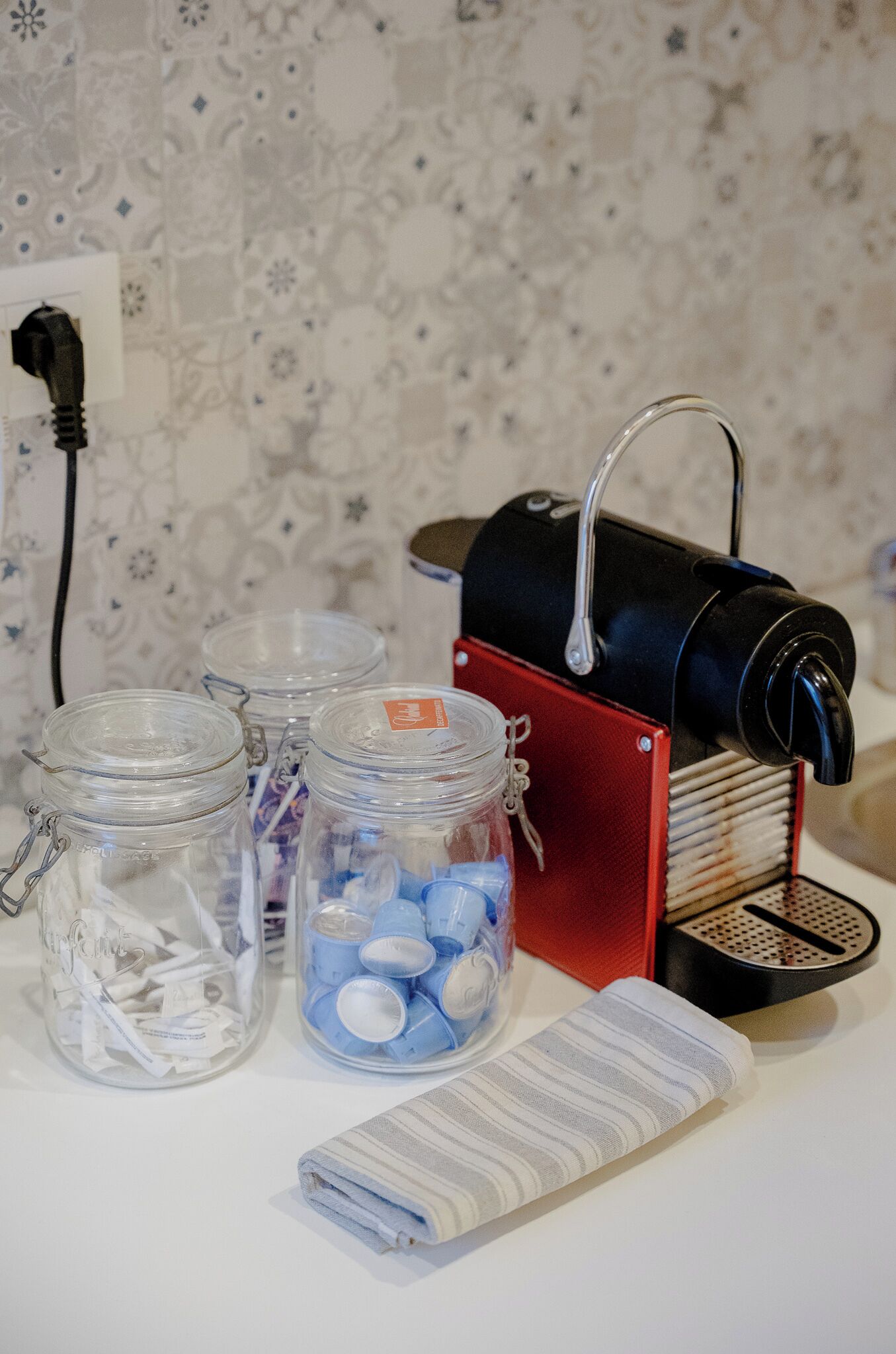 A coffee maker, two glass jars with lids, and a striped cloth on a table.