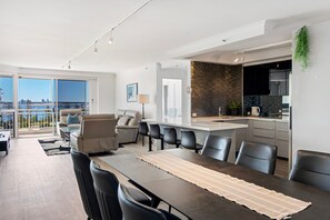 A modern apartment with a dining area, kitchen, and a balcony with a city view. - Ocean Sands Central Main Beach Apartment (Main Beach)