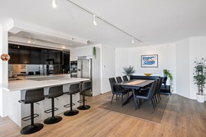 A modern kitchen with a central island, bar stools, and a dining area with a table and chairs. - Ocean Sands Central Main Beach Apartment (Main Beach)