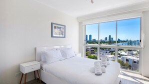 Ein Hotelzimmer mit einem großen Bett, einem Nachttisch, einem gerahmten Bild an der Wand und einem Fenster mit Blick auf die Stadt.
