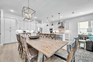 A modern kitchen with white cabinetry, a wooden dining table, and pendant lighting. - Beach Please by Stay on 30a (Inlet Beach)